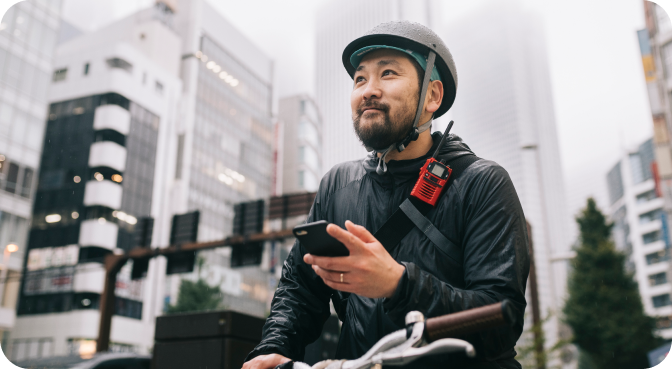Man wearing bike helmet and rain gear, standing over a bike and smiling, cell phone in hand