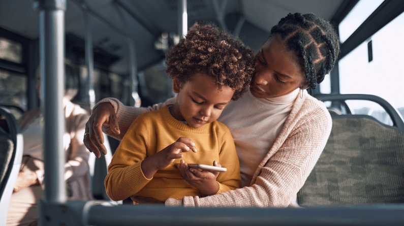 A child sits on the lap of a parent while riding the bus